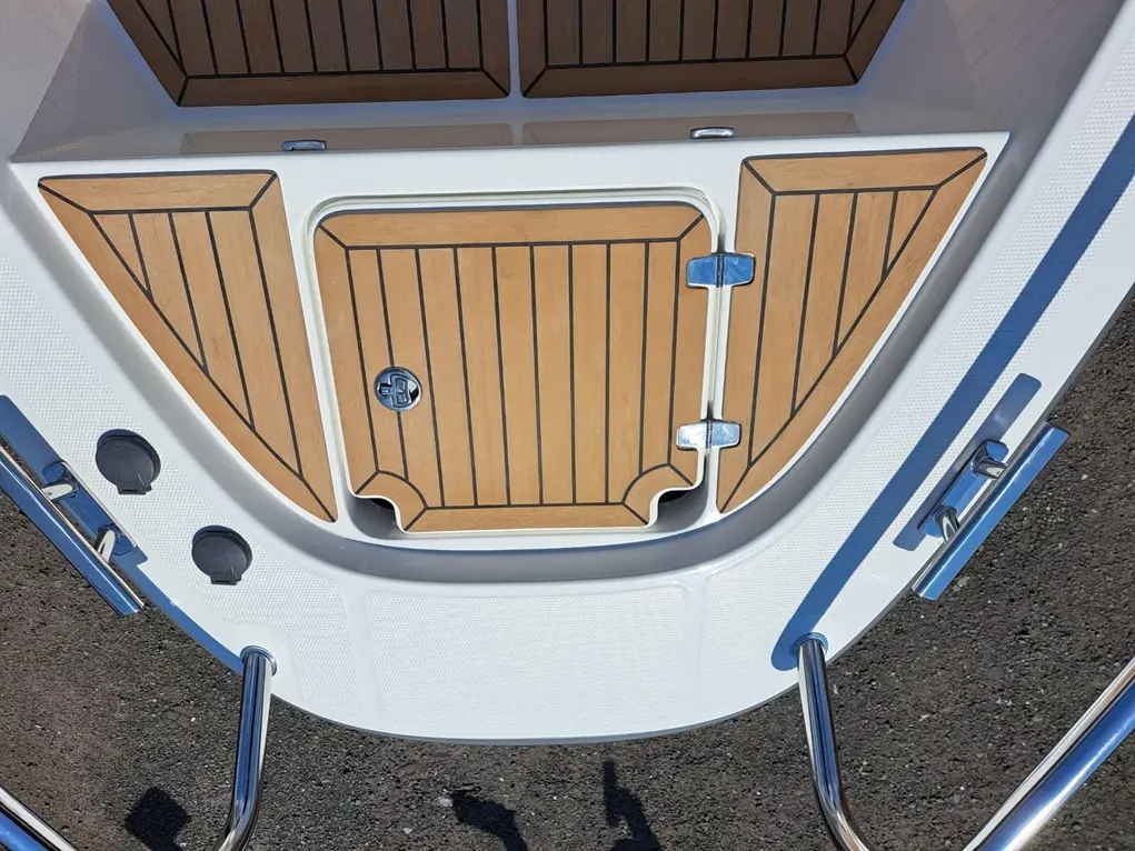 Top view of a boat's deck featuring wooden accents, a closed hatch, and metal handles along with two black fittings.